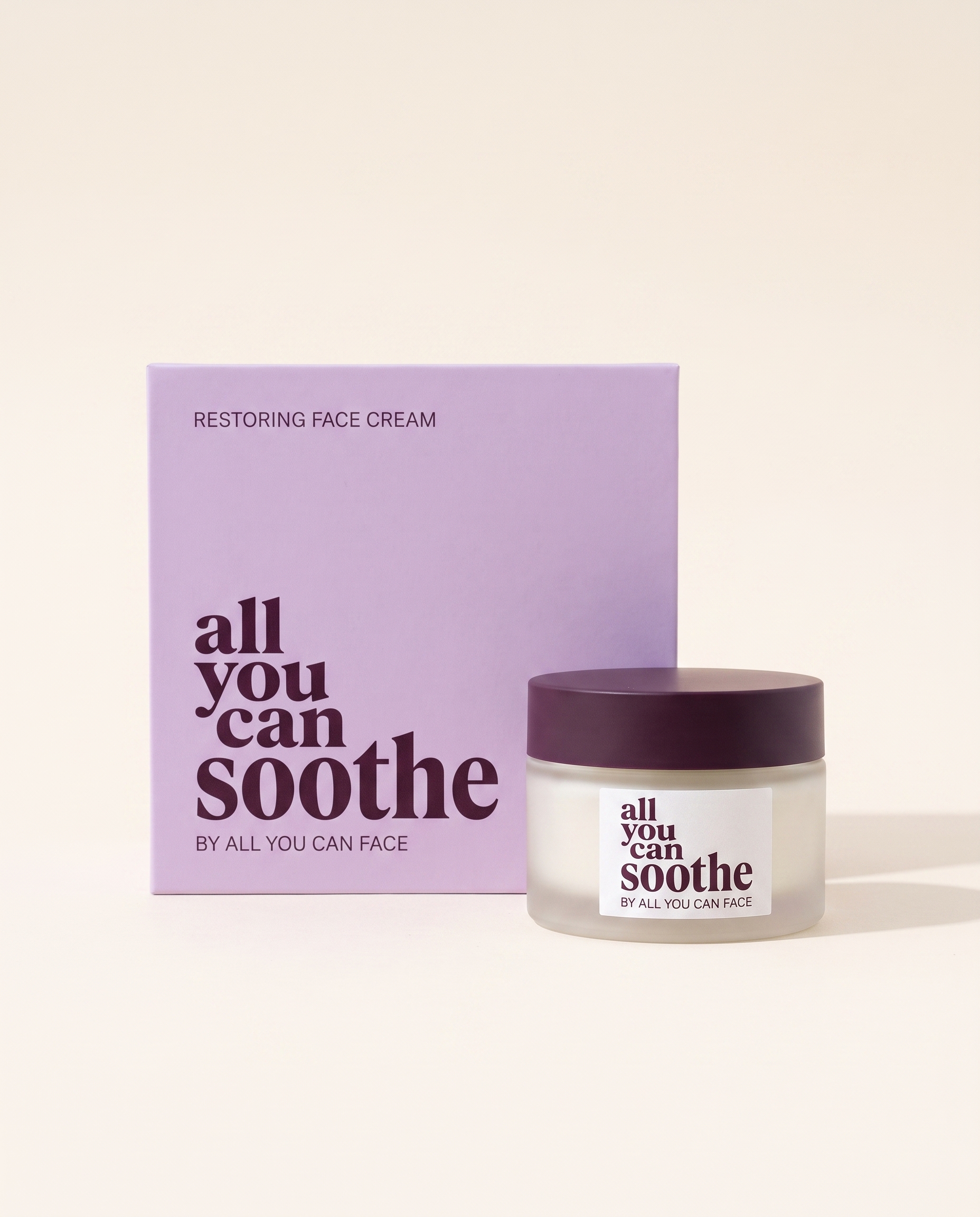 Ein Tiegel aus mattem Glas mit pflaumenfarbenem Deckel und dem Etikett „all you can soothe", vor seiner fliederfarbenen Schachtel auf sandfarbenem Papier.