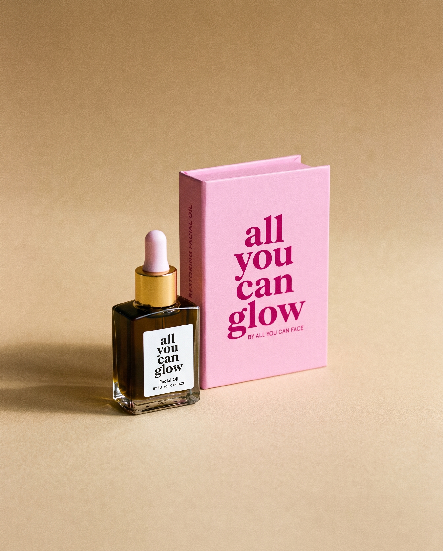 Die Pipettenflasche „all you can glow" aus dunklem Glas mit weißem Etikettenfeld und goldenem Kragen, vor ihrer rosa Schachtel auf sandfarbenem Papier.